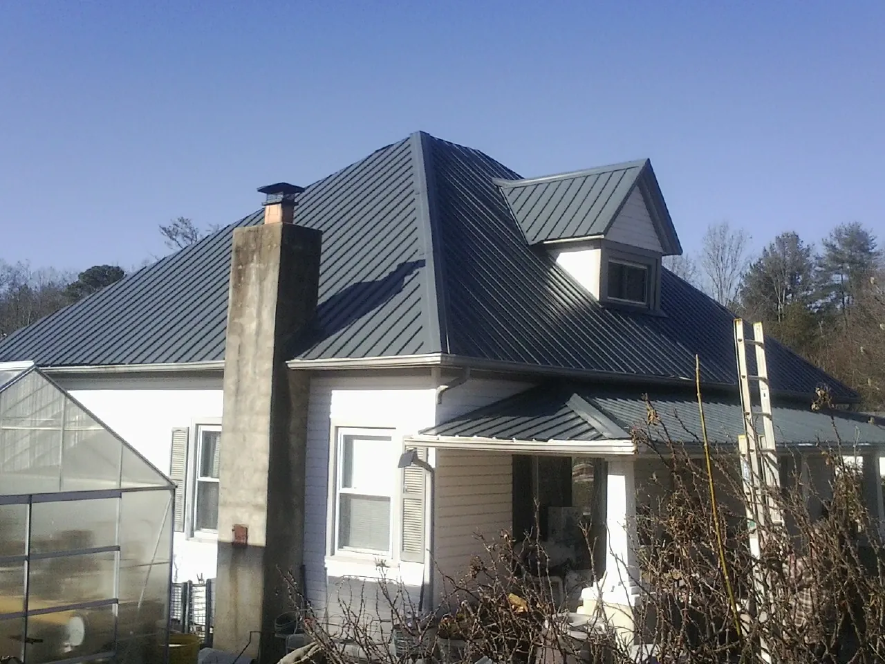 Dark blue standing seam metal roof on a white farmhouse with dormer — Slate & Tile Roof Repair by Roofing Brothers in Cannonville