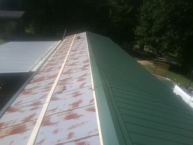 Old rusted panels beside newly installed green metal roofing — Wind Damage Roof Repair by Roofing Brothers in Cannonville