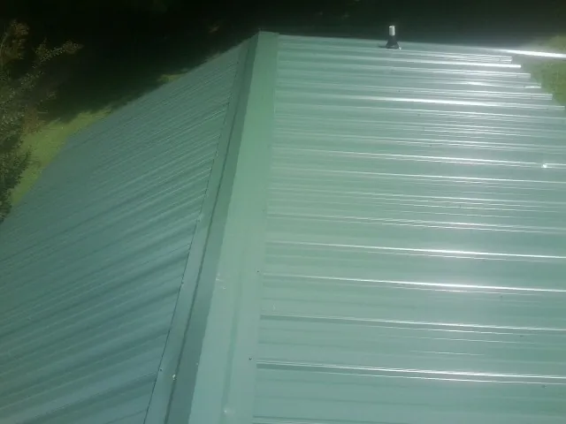 New green metal panels meeting at the ridge of a roof — Flat Roof Repair work by our crew in Cannonville