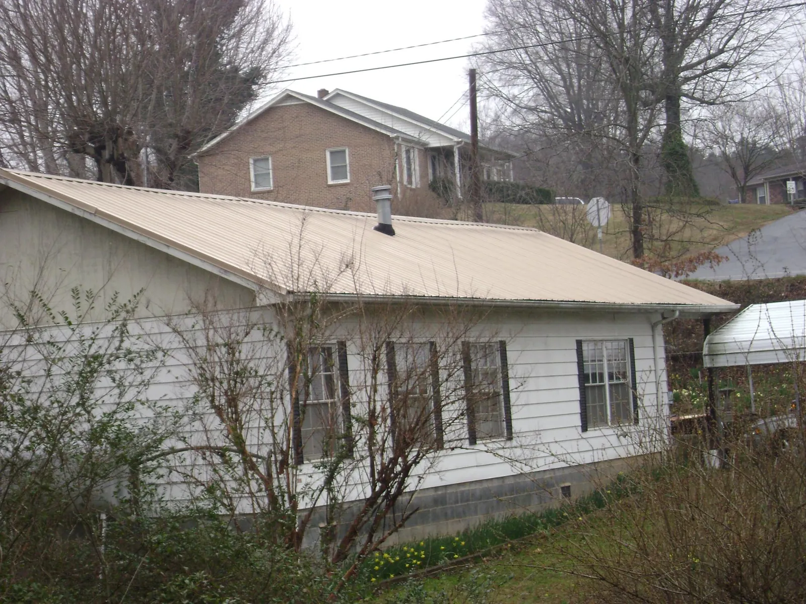 Tan metal roof on a white sided house set into a hillside — Commercial Roofing by Roofing Brothers in Cannonville
