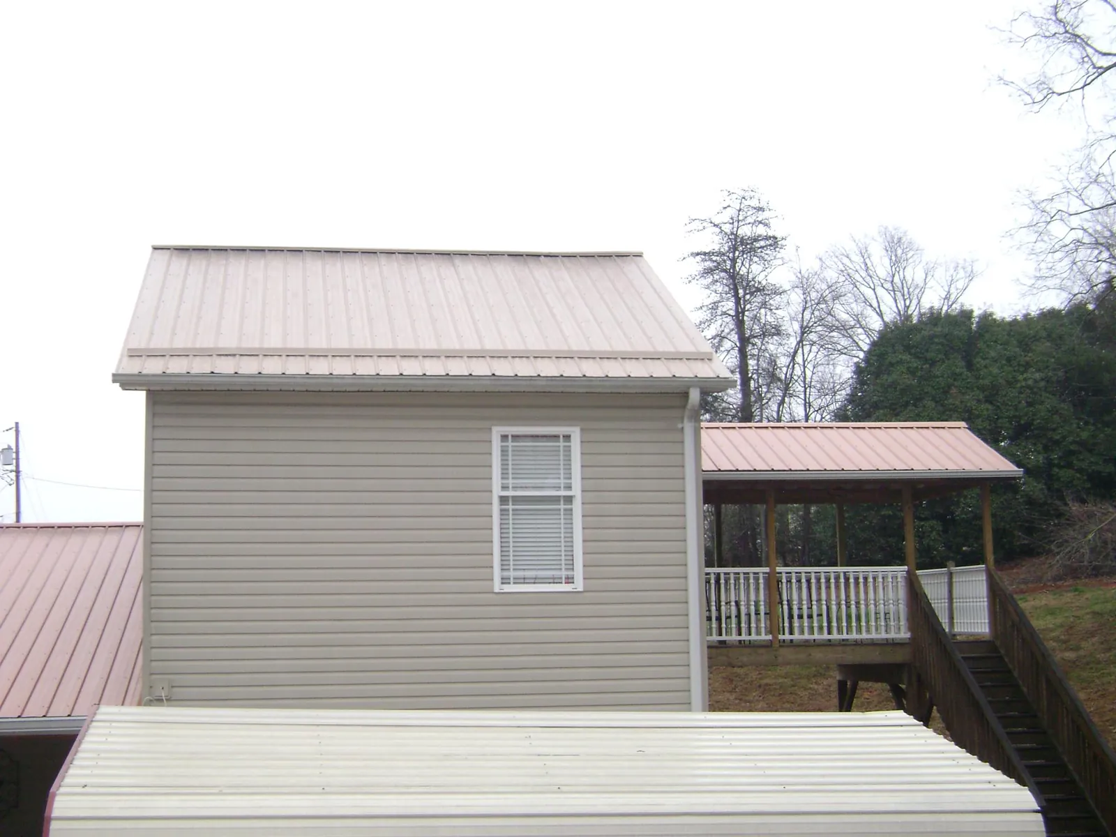 Tan metal roofs on a two story addition and attached porch, from a Roof Replacement job in Cannonville